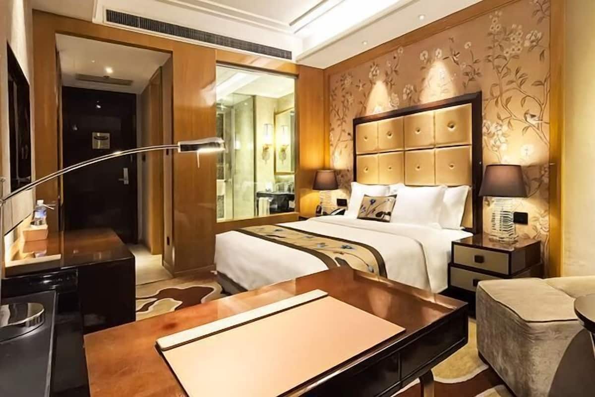 A hotel room with a large bed, a wooden desk, a nightstand, and a chair.