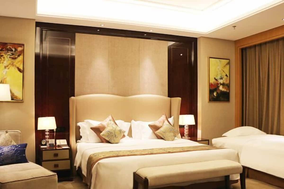 A hotel room with a large bed, a smaller bed, a bench, and two bedside tables with lamps.