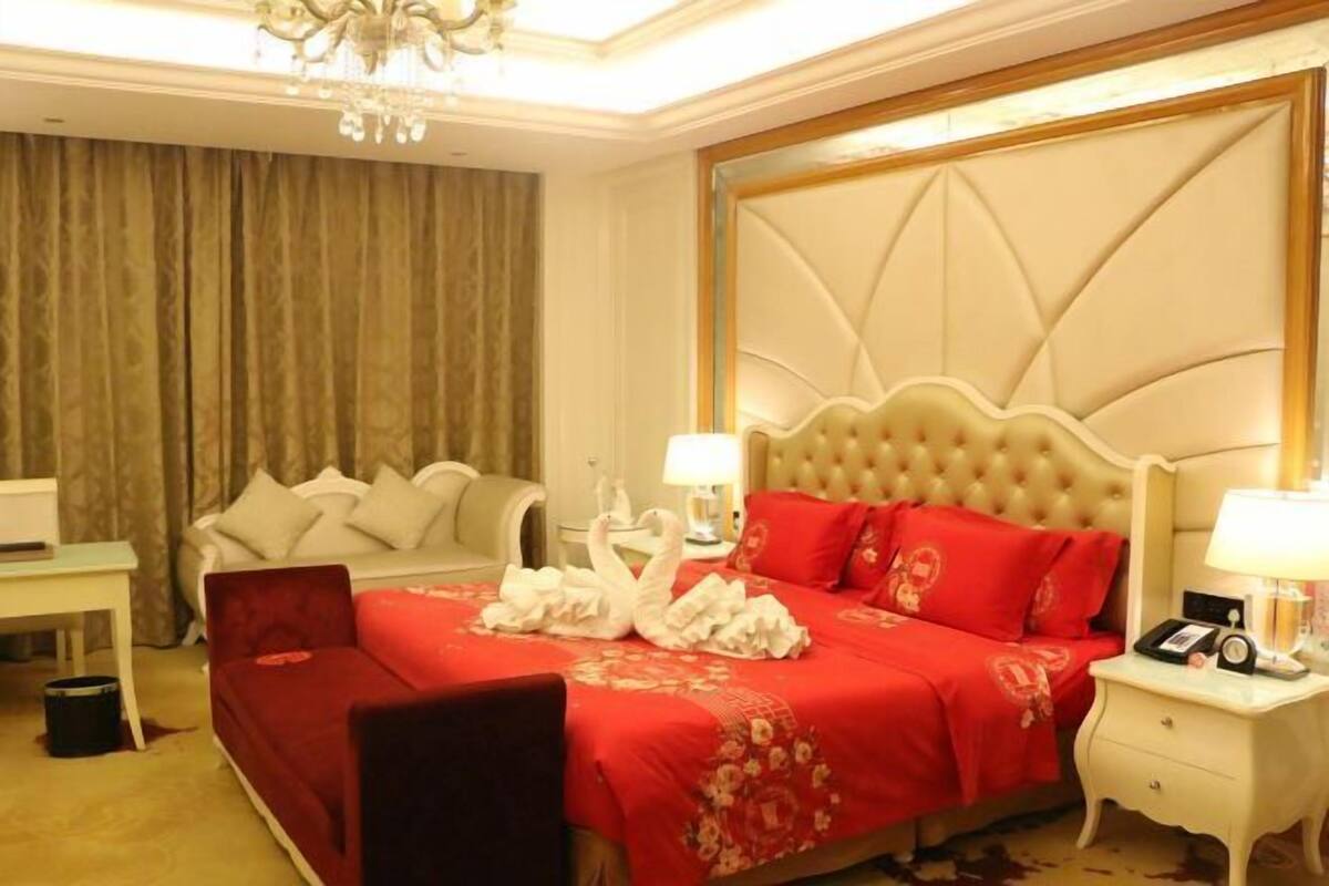 A hotel room with a large bed, a desk, a chair, and a chandelier.