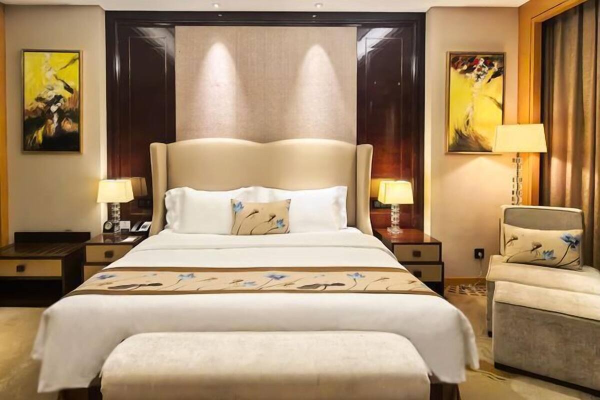A hotel room with a large bed, two bedside tables with lamps, a chair, and artwork on the walls.