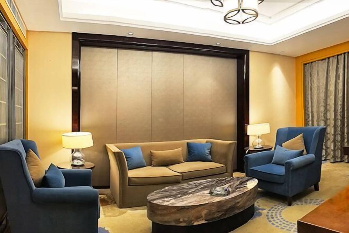 A modern hotel room with a sofa, armchairs, a coffee table, and a large window.