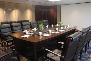 Un salón de conferencias con una larga mesa, varias sillas y una pantalla para proyector.