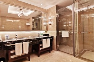 Un baño moderno con un espejo grande, tocador oscuro, dos toallas, cabina de ducha de vidrio y suelo de mármol.