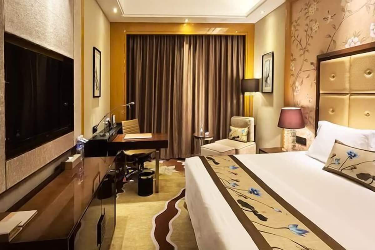 A hotel room with a bed, desk, chair, TV, and curtains.