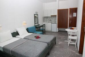 A compact hotel room with two beds, a kitchenette, a small dining table, and a bathroom.