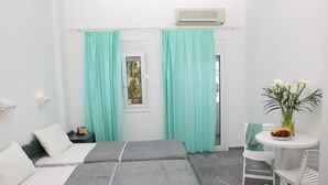 A small, clean room with two beds, a table with a vase of flowers, and a window with curtains. - La Palma III (Malevizi)