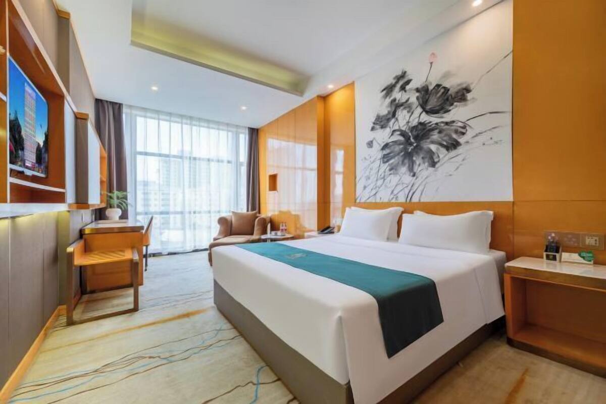 A hotel room with a large bed, a desk, a chair, and a wall-mounted TV.