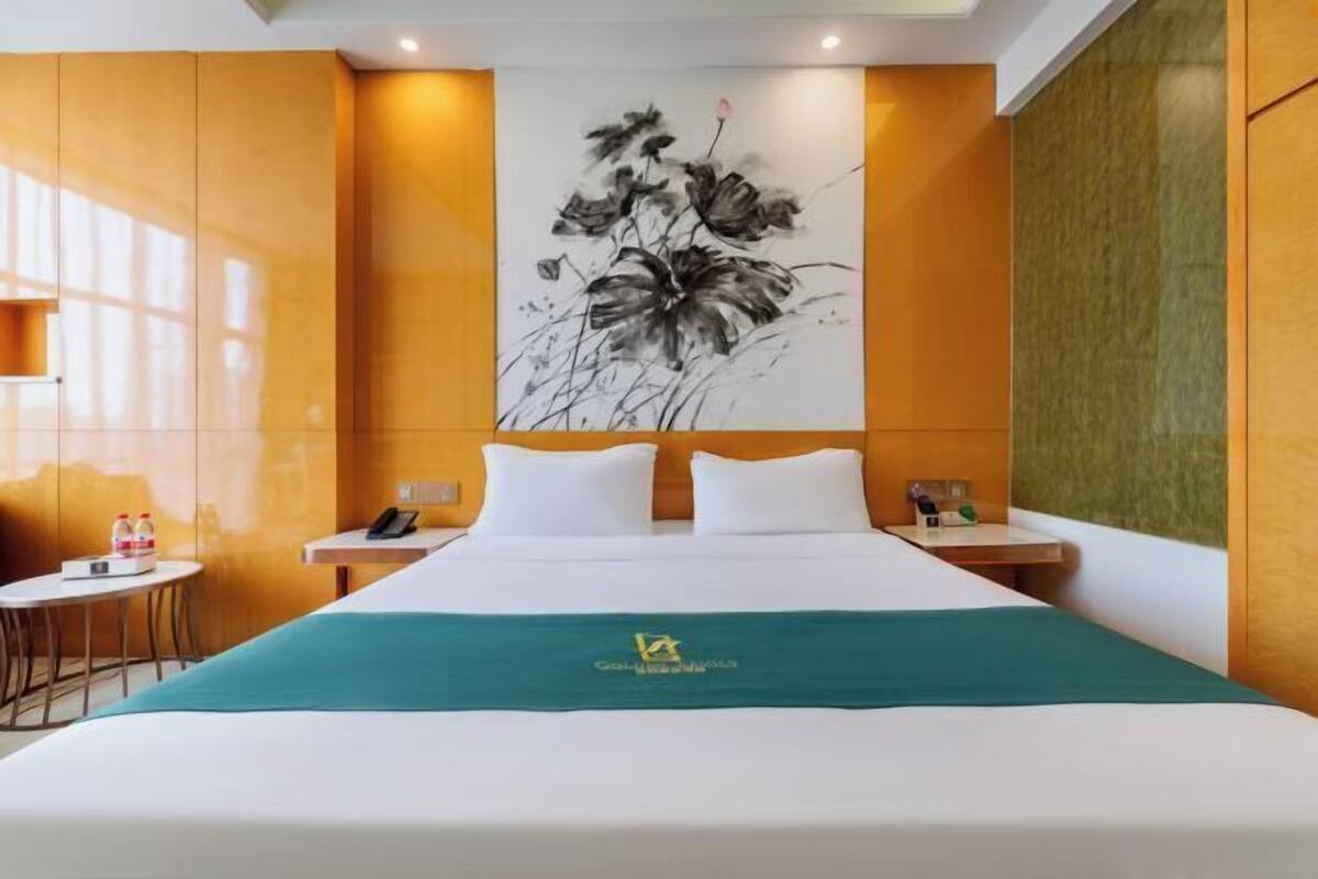 A hotel room with a large bed, a desk, a chair, and a wall-mounted artwork.