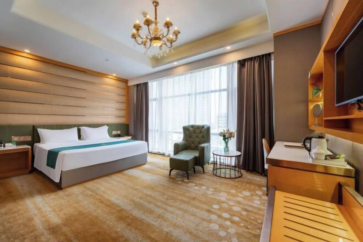 A hotel room with a bed, a chair, a small table, a TV, and a chandelier.