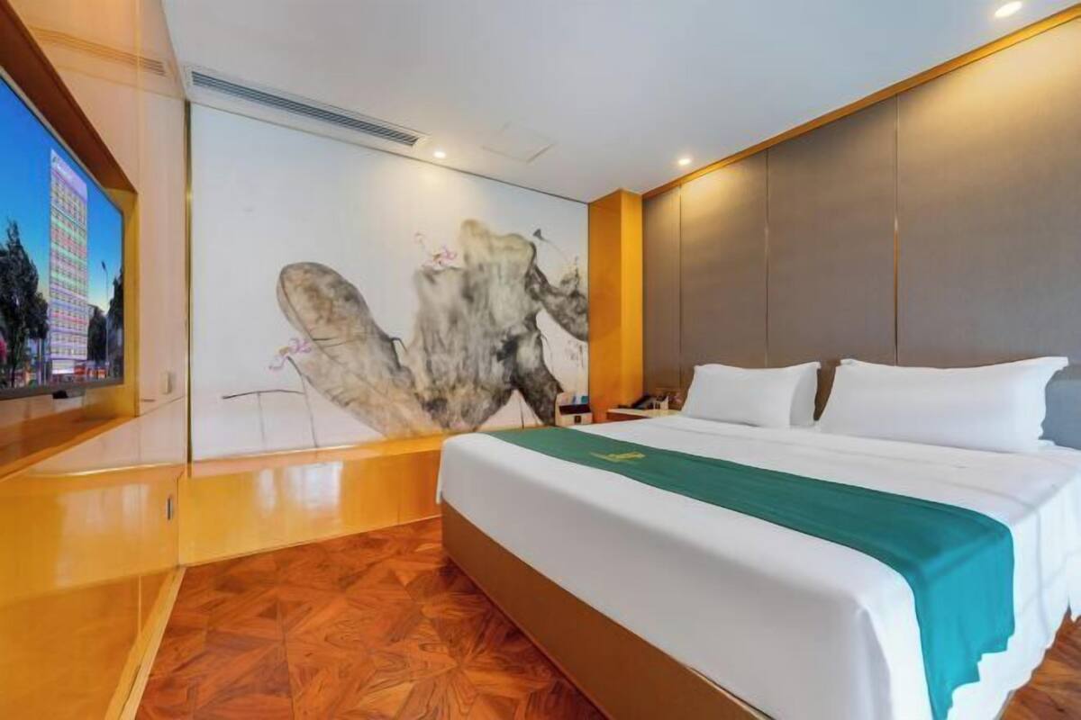 A hotel room with a bed, a large wall mural, a television, and a wooden floor.