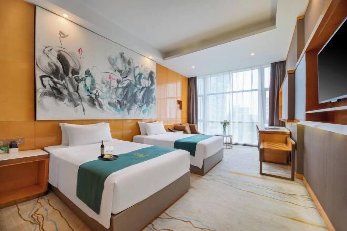 A hotel room with two beds, a large abstract painting on the wall, a TV, and a view of the city through large windows.
