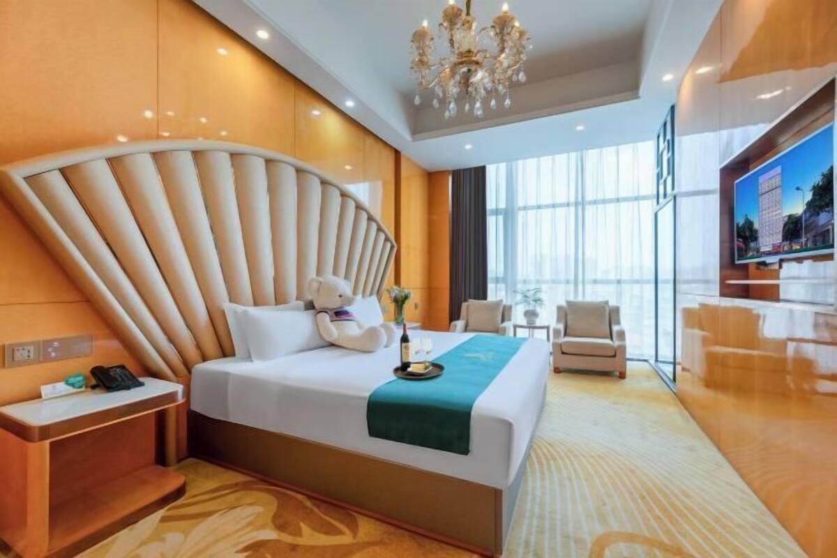 A modern hotel room with a large bed, a desk, a chair, a TV, and a view of the city.