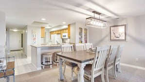 A modern kitchen with white cabinets, a central island, and a dining area with a wooden table and white chairs.