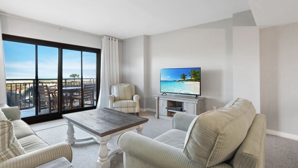 A hotel room with a balcony, a television, a dining table, and two armchairs.