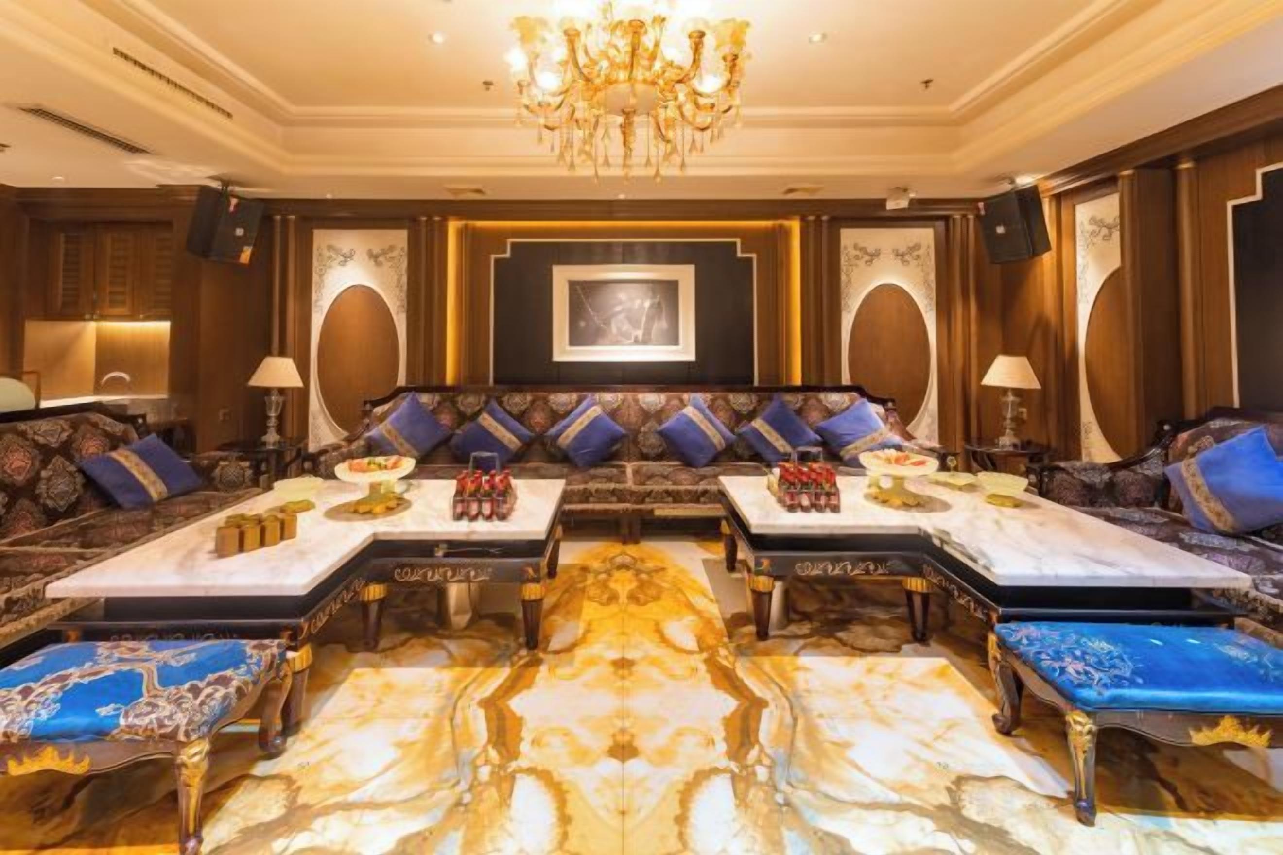 A luxurious lounge area with a central sofa set, a chandelier, and a patterned floor.