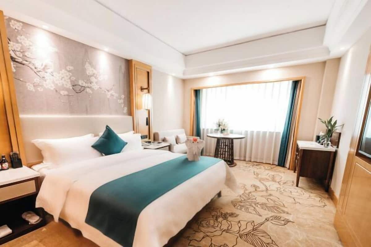 Ein Hotelzimmer mit einem großen Bett, einem kleinen Tisch, einem Stuhl und Blick ins Freie.
