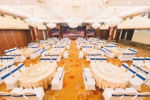 A banquet hall with round tables and chairs, a chandelier, and a stage with a banner. - Shen Long Hotel (Hengyang)