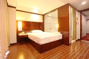 A hotel room with a large bed, a nightstand, a mirror, and a wooden floor. - Shen Long Hotel (Hengyang)
