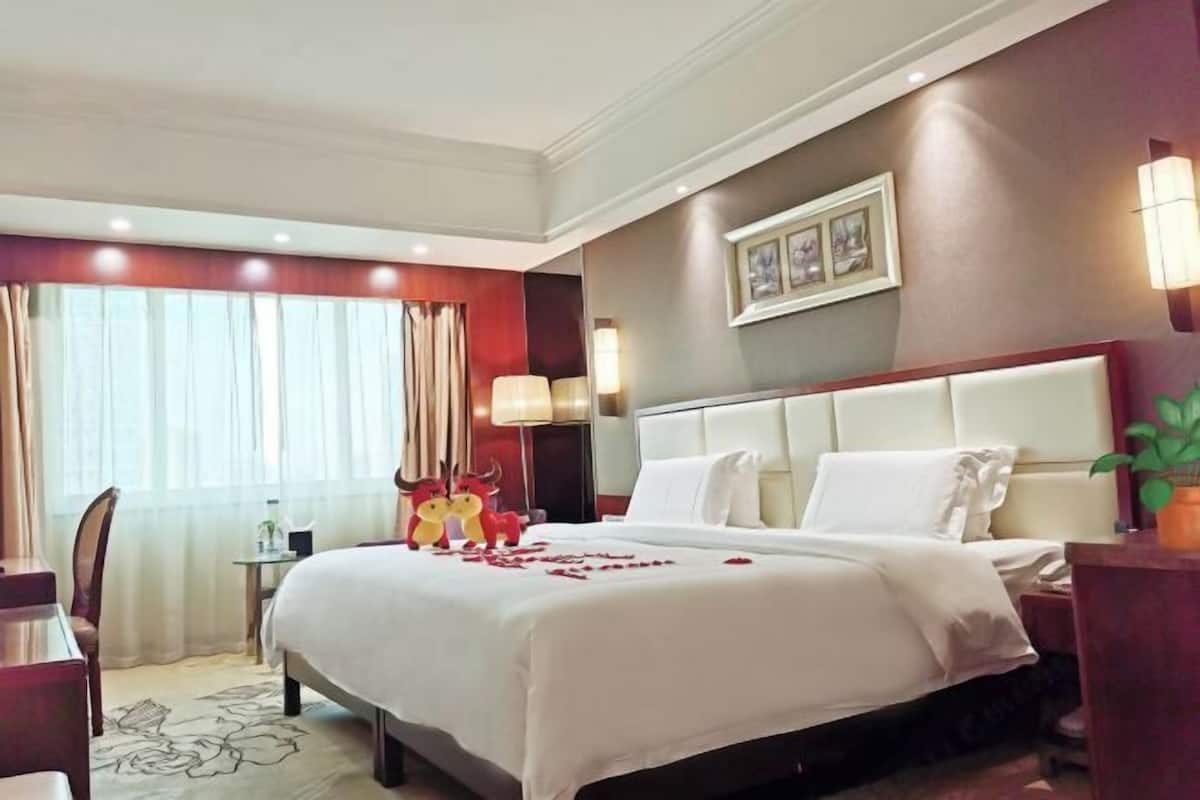 Ein Hotelzimmer mit einem großen Bett, einem Schreibtisch, einem Sessel, einem kleinen Tisch und einer Wandlampe.