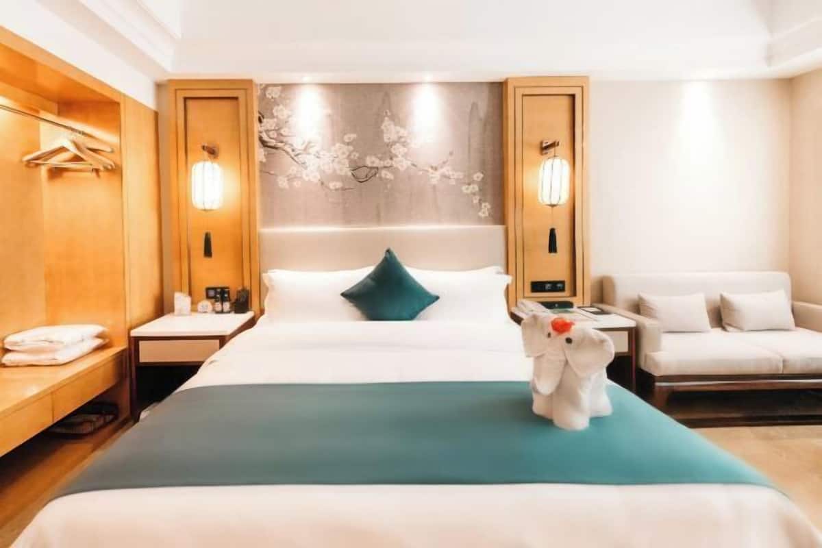 Ein Hotelzimmer mit einem Bett, einem Schreibtisch, einem Stuhl, einem Kleiderhaken und einer Wandleuchte.