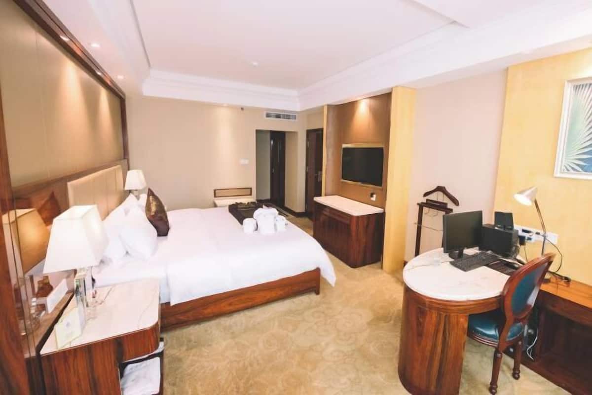 Ein Hotelzimmer mit einem Bett, einem Schreibtisch, einem Stuhl, einem Spiegel und einem Fernseher.