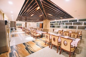 A spacious dining area with multiple tables and chairs, a modern ceiling design, and a kitchen area in the background. - Shen Long Hotel (Hengyang)