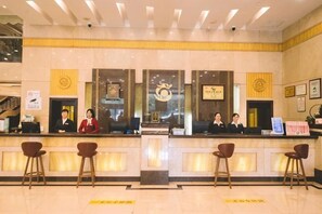 Zona de recepción de un hotel con mostrador, taburetes de bar y personal de recepción.