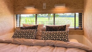 Une chambre à coucher avec un lit, des coussins à motifs, une fenêtre donnant sur un champ verdoyant et un mur à texture.