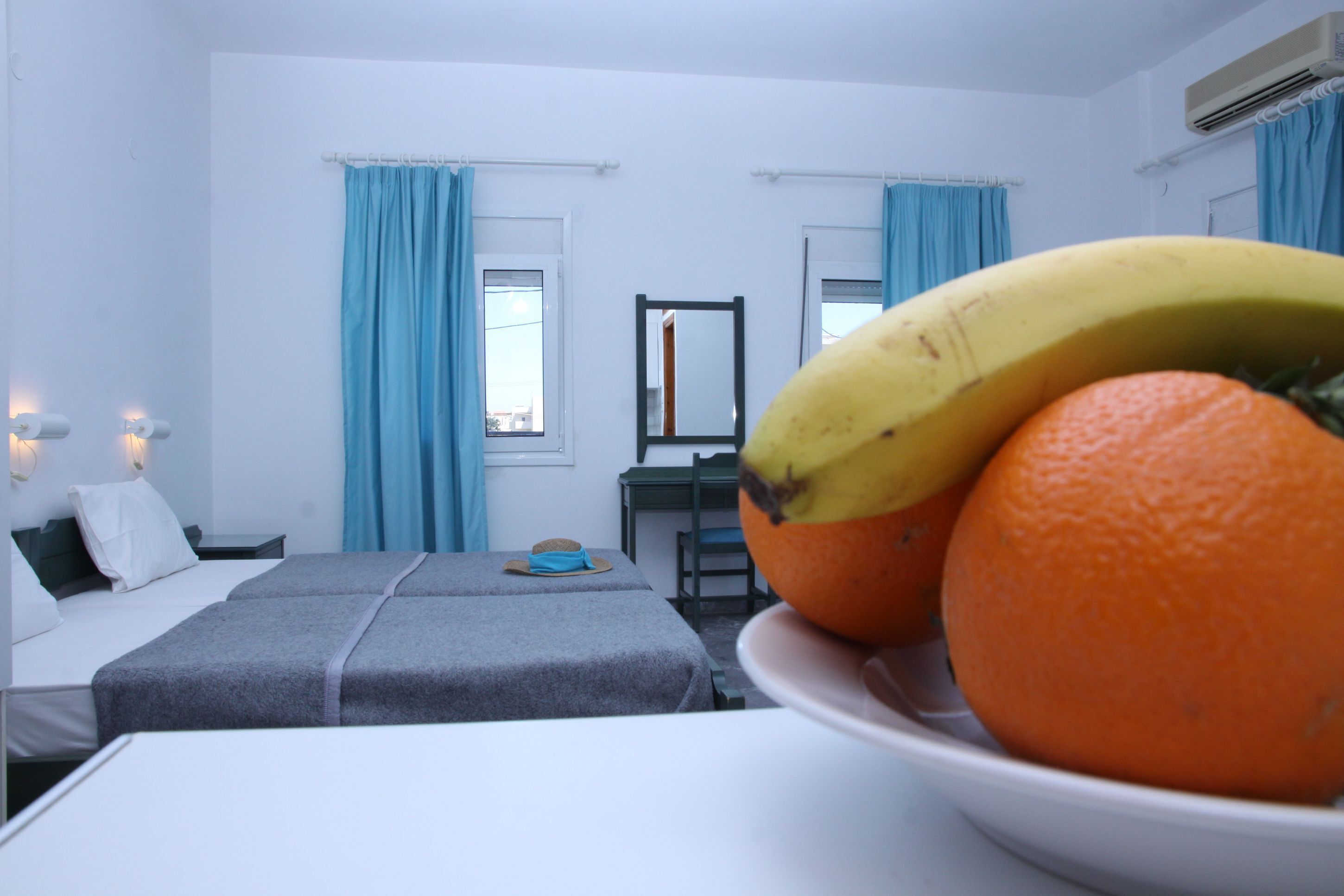 A hotel room with a bed, a desk, a mirror, and a bowl of fruit.