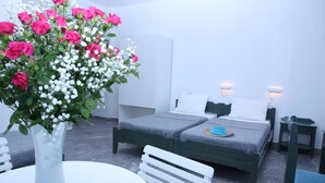 Ein Schlafzimmer mit einem Bett, Nachttischen, einem Sessel, einem kleinen Tisch und einer Vase mit Blumen.
