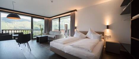 A modern hotel room with a large bed, a desk, and a balcony with a view of the hills.