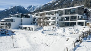 Um hotel moderno de vários andares com grandes janelas e varandas, com as montanhas nevadas ao fundo.