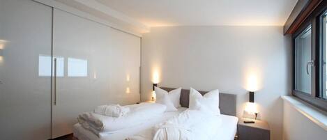 A modern hotel room with a large bed, bedside tables, and a wardrobe.