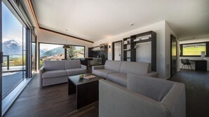 Uma sala de estar moderna com um sofá grande, uma mesa de centro e vista para montanhas através de amplas janelas.