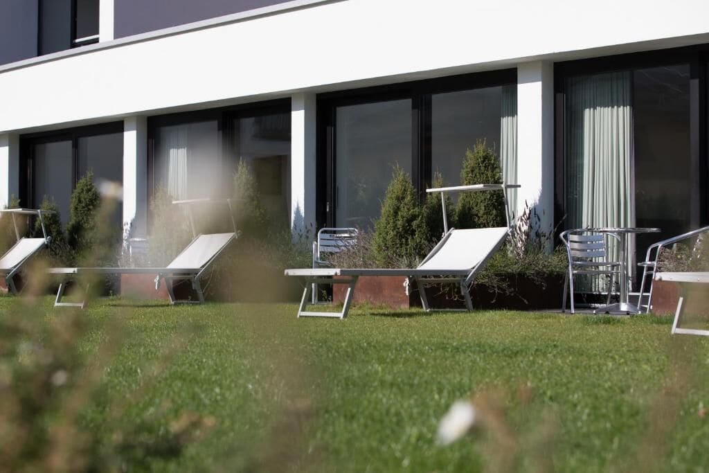 A modern building with multiple lounge chairs aligned along the side, large windows, and a well-maintained lawn.