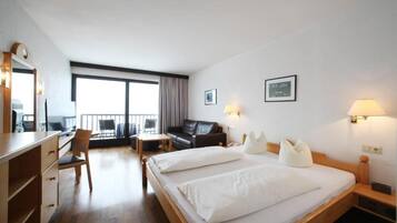 Habitación de hotel con una cama grande, un escritorio, una silla, un sofá y un balcón con vistas.