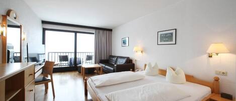 Habitación de hotel con una cama grande, un escritorio, una silla, un sofá y un balcón con vistas.