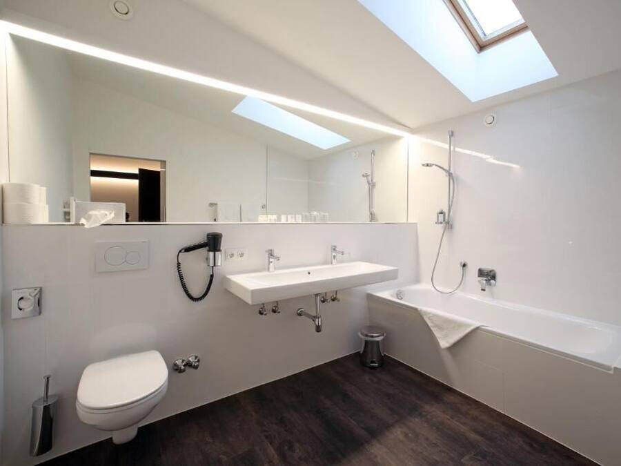 Un baño moderno con tragaluz, un lavabo blanco, inodoro y bañera.