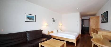 A compact hotel room with a bed, a sofa, a small table, and a desk.