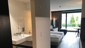 Quarto de hotel moderno com uma cama grande, espaço de estar separado e vista para o exterior.