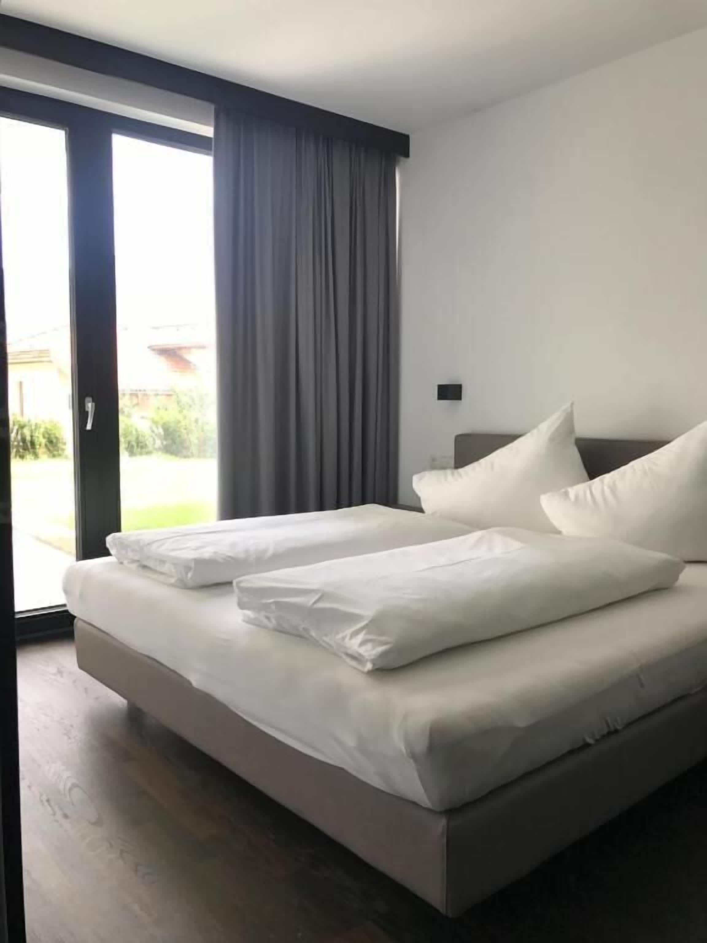 A modern hotel room with a large bed, grey curtains, and a view of the outdoors.