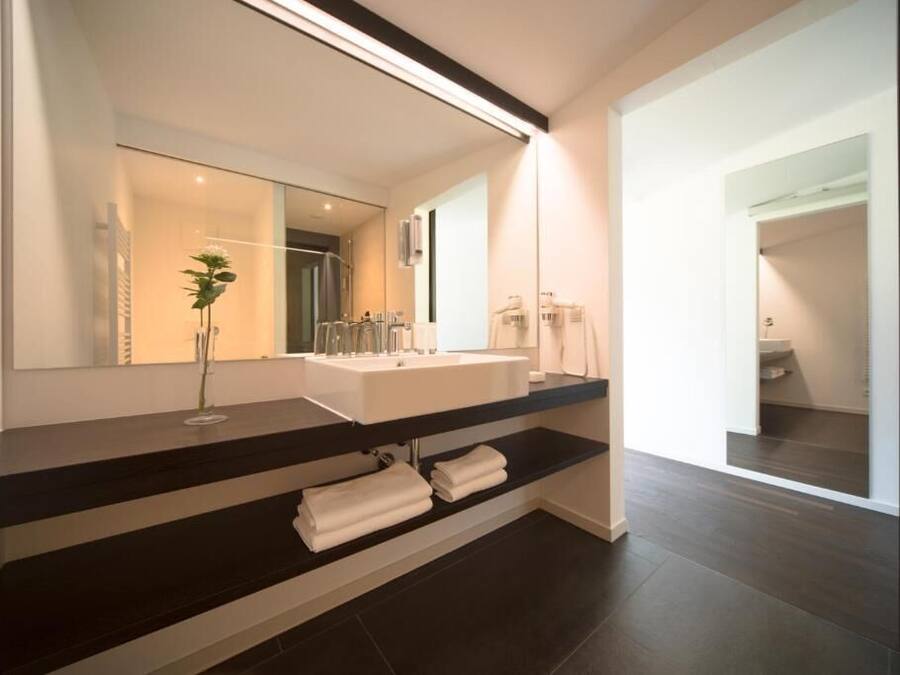 A modern bathroom with a large mirror, a white sink, and a dark countertop.