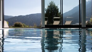 Piscina interna com água cristalina, rodeada por amplas janelas que oferecem vista para montanhas e vegetação.