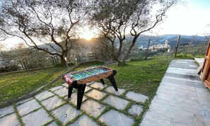 An outdoor foosball table set on a stone patio with a view of trees and distant buildings.