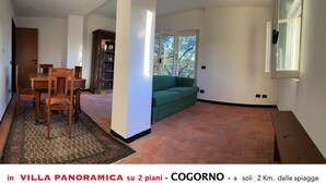 A spacious living room with a wooden table and chairs, a green sofa, and a large window. - Apartment An in panoramic villa (San Salvatore)