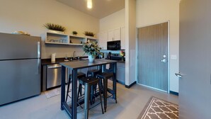 Une cuisine moderne dotée d’un îlot central intégré, d’appareils électroménagers en acier inoxydable et d’un four à micro-ondes. L’îlot est agrémenté de tabourets de bar, et une porte donne accès à une autre pièce.
