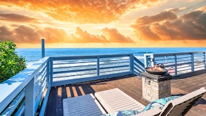 A wooden deck with a railing overlooking the ocean, a stone fireplace, and lounge chairs. - Single Family Beachfront Home with a Spa P2031-0 (Oceanside)