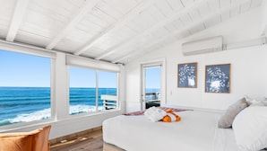 A bedroom with a large window overlooking the ocean, a bed with pillows, and a wooden floor. - Single Family Beachfront Home with a Spa P2031-0 (Oceanside)