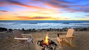 A beach scene with two wooden chairs and a campfire between them, overlooking the ocean. - Single Family Beachfront Home with a Spa P2031-0 (Oceanside)