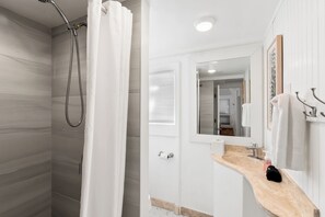 A modern bathroom with a shower, a vanity with a wooden countertop, a mirror, and a towel rack. - Single Family Beachfront Home with a Spa P2031-0 (Oceanside)